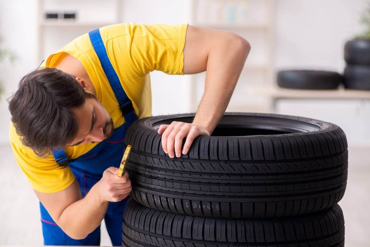 Meccanico che ispeziona attentamente il battistrada del pneumatico con una lente d’ingrandimento in officina