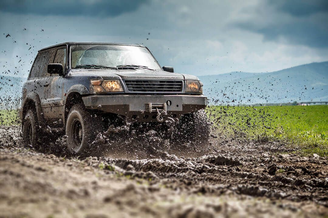 SUV with off-road tires splashing mud while driving on dirt